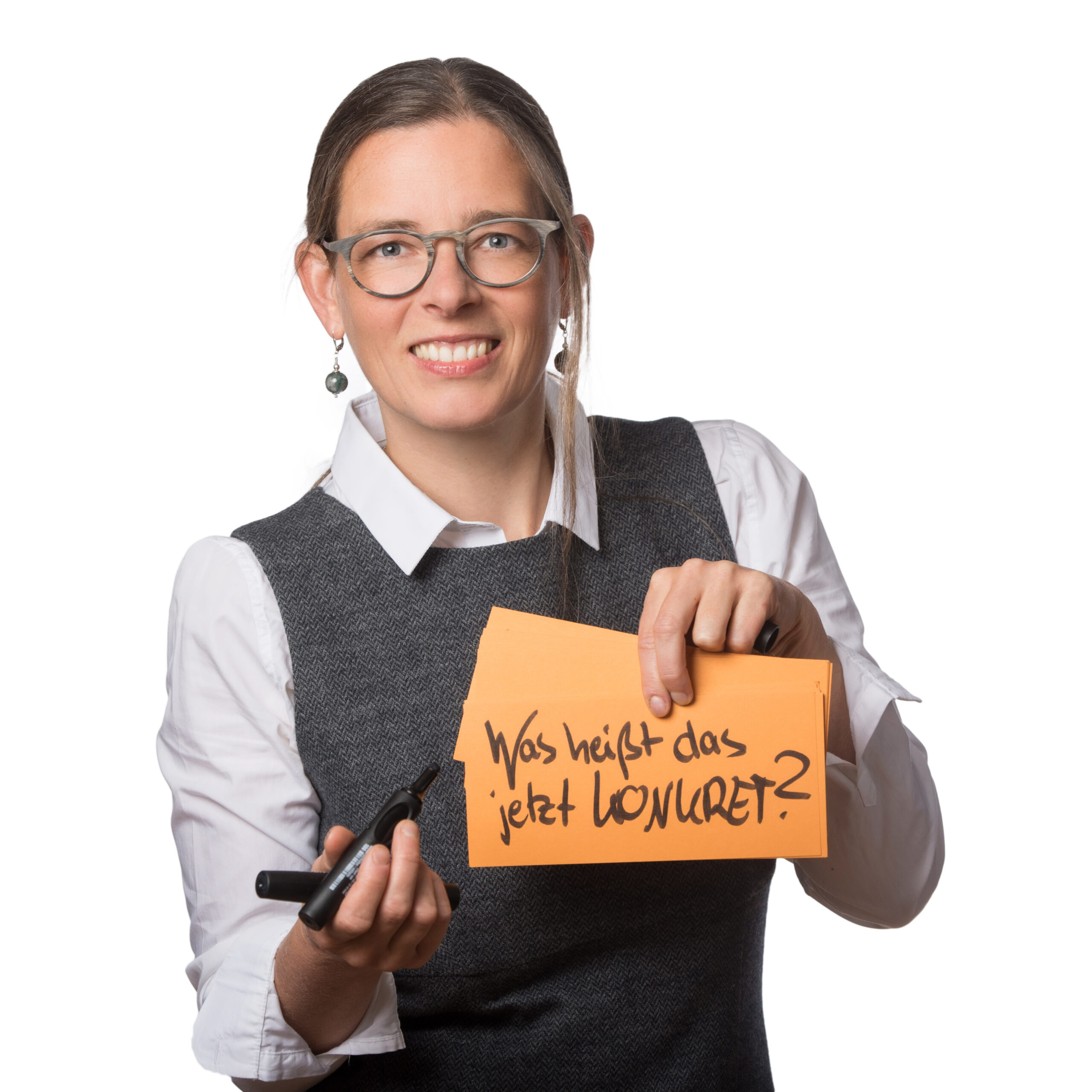 Claudia Christ mit dem Schild 'Was heißt das jetzt KONKRET?' für Impulse & Fortbildung